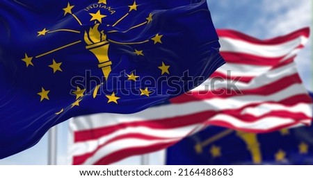 The Indiana state flag waving along with the national flag of the United States of America. In the background there is a clear sky. Indiana is a U.S. state in the Midwestern United States Royalty-Free Stock Photo #2164488683