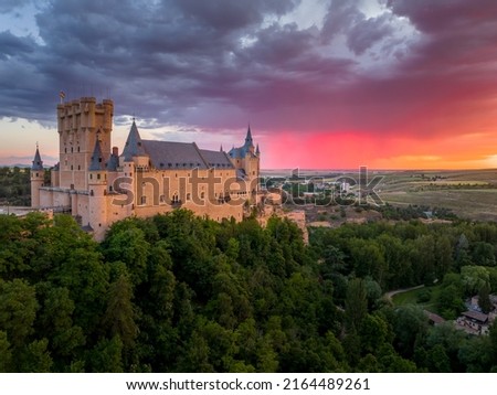Sunset over the Alcázar of Segovia medieval castle in Castile and León, Spain. Rising out on a rocky crag above the confluence of two rivers with majestic red, orange, yellow as the sun paints the sky Royalty-Free Stock Photo #2164489261