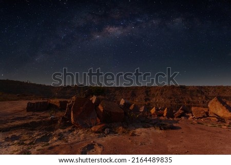 Milky Way over a lake in a granite quarry at night. Summer landscape with huge boulders, trees, purple sky with milky way and stars, beautiful reflection in the water. Ukraine. Space and nature.