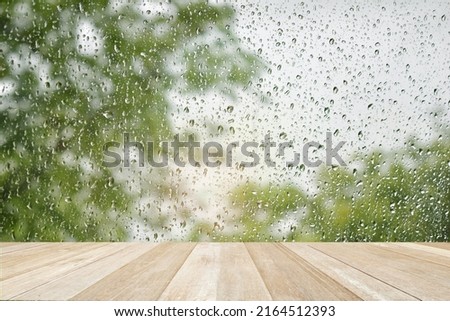 Empty top wooden table on drops of the rain on blurred green nature