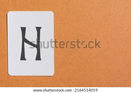 Still life photo of a white card stock, with a rune printed on it, specifically the rune is Hagalaz