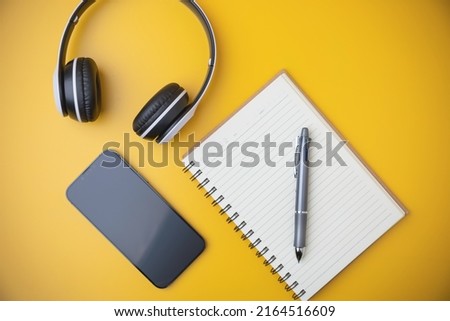 Technology, Audio music of multimedia for relaxing. Top view, flat lay. a black and white headphones a notebook with a smartphone on a yellow background with copy space.