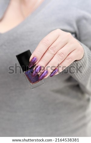 Female hand with long nails and purple plum manicure holds a bottle of nail polish