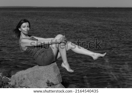 Beautiful slender woman sitting on a rock by the sea in black and white