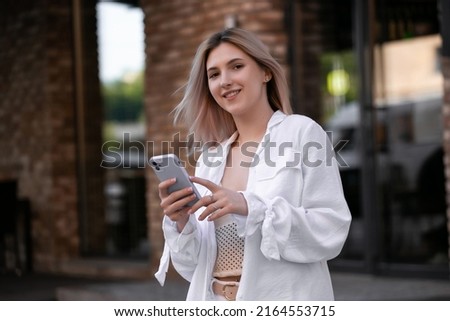 gorgeous beautiful young woman with blonde hair messaging on the smart-phone at the city street background. pretty girl having smart phone conversation on city street.