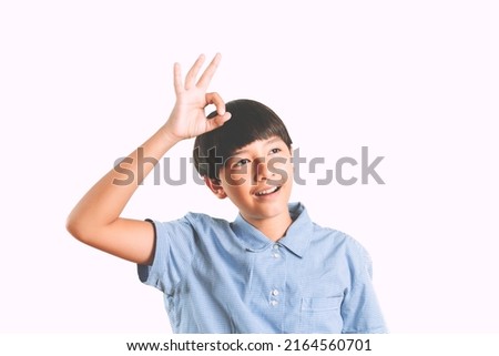 A portrait of a smiling smart boy shows okay gesture confirmation or approval gesture expresses positive emotions looks at the camera over white background. It is fine, thank you. Hand sign.