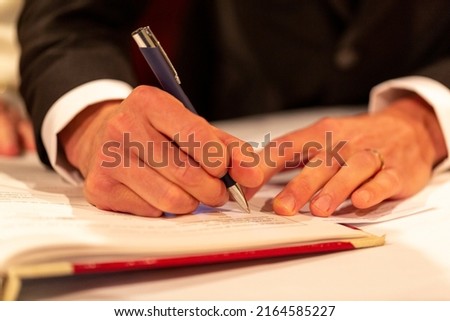 hands of groom signs marriage deed in Christian ceremony. High quality photo