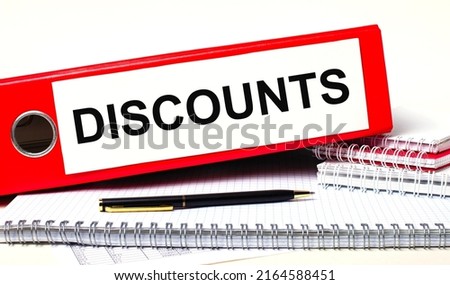 On the desktop are notebooks, a pen and a red folder for papers with the text DISCOUNTS. Business concept