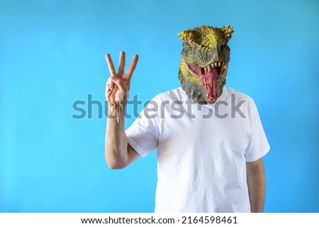 Funny laughing dinosaur head on human body on white t-shirt on blue background, showing three fingers with the hand, Clip art, negative space.