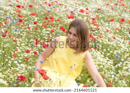 a beautiful young blonde woman in a yellow dress stands among a flowering field