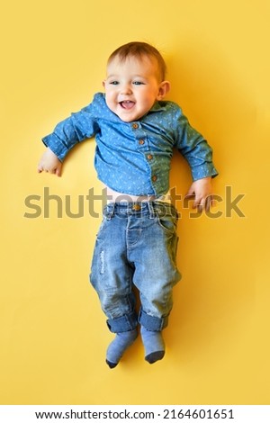 A happy child on a studio yellow background in a blue shirt and pants. Smiling infant baby boy in jeans