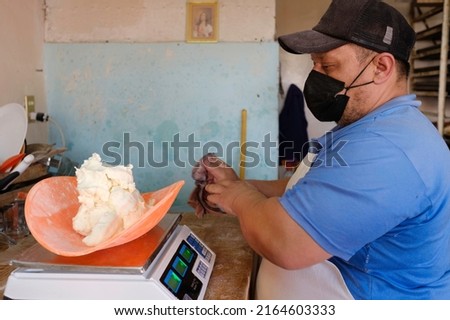 Latin baker with mask, working weighing flour dough to make bread. Traditional Mexican bakery.
