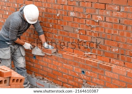 Bricklayer laying bricks on mortar on new residential house construction Royalty-Free Stock Photo #2164610387