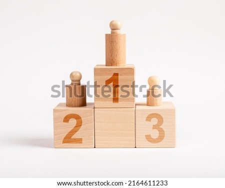 Winners podium from wooden blocks with knobbed cylinders and numbers 1, 2, 3. Hierarchy, ranking concept. Distribution of places among competition champions. High quality photo Royalty-Free Stock Photo #2164611233