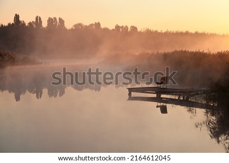 Foggy morning over calm river, pink fog against morning sun, fisherman place. Ukraine, peace.