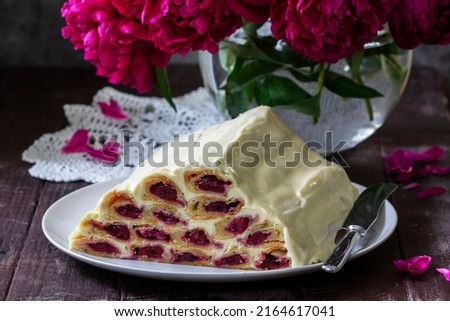 Cake Monastic hut with cherry filling and sour cream, a bouquet of peonies on a wooden table.