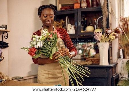 African American female florist making a bouquet of fresh flowers while working at flower shop. Royalty-Free Stock Photo #2164624997