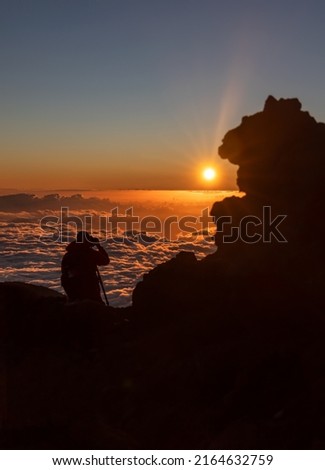 Sunset landscape above the clouds with silhouette of a photographer and a rock formation. Peak of Mount Teide called 'Pico del Teide'. Teide National Park, Tenerife, Canary islands, Spain.