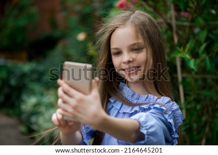 Cute little girl takes selfie by smart phone outside. Kid uses modern technology. Child listen music and dancing.