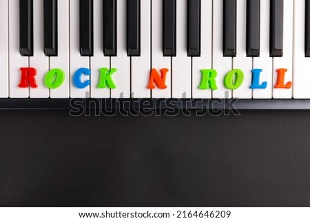 The word Rock n roll is composed of multicolored letters on the piano keys. Copy space.	