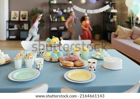 Horizontal image of candy bar on table with donuts, cupcakes and popcorn with group of children running in background