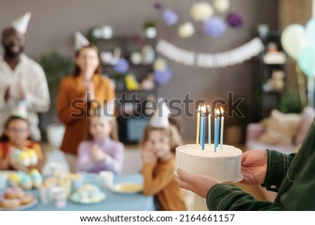 Close-up of father carrying cake with burned candles to congratulate his son with birthday