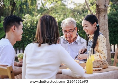 Happy Asian family eating a meal together at home garden. Outdoor dinner party