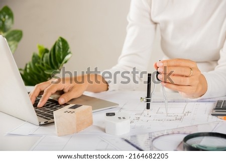 Architectural project workplace. Architect typing laptop keyboard to review design of house building before editing or sketching with compass on blueprint paper on table desk at architecture office