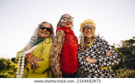 Stylish senior women smiling at the camera while standing together in a park. Group of confident elderly women wearing colourful casual clothing. Three mature women enjoying their golden years. Royalty-Free Stock Photo #2164682873