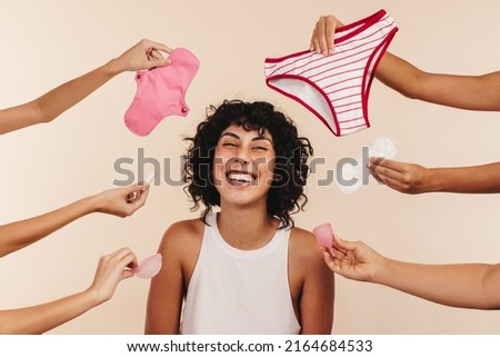 Making the right feminine hygiene choice. Happy young woman smiling at the camera while surrounded by hands holding different disposable and non-disposable sanitary products. Royalty-Free Stock Photo #2164684533