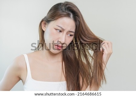 Damaged Hair, frustrated asian young woman, girl hand in holding splitting ends, messy unbrushed dry hair with face shock, long disheveled hair, health care of beauty. Portrait isolated on background. Royalty-Free Stock Photo #2164686615