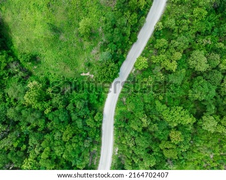 Aerial view of countryside road passing through the green forrest and mountain in Thailand.