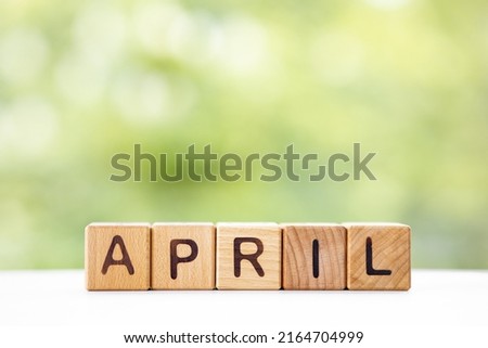 The word April on wooden cubes. They lie on other cubes against the backdrop of the summer garden. Month of year
