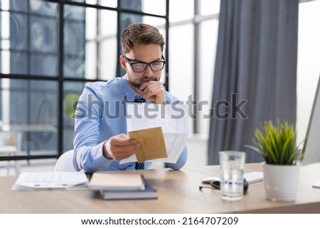 Handsome entrepreneur reading a letter from envelope in a desktop at office