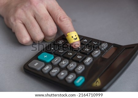 Man's index finger presses calculator button. Man does math on calculator. The index finger is wrapped in yellow ribbon. Happy smiling face drawn on finger. Happy Positive emotion concept.