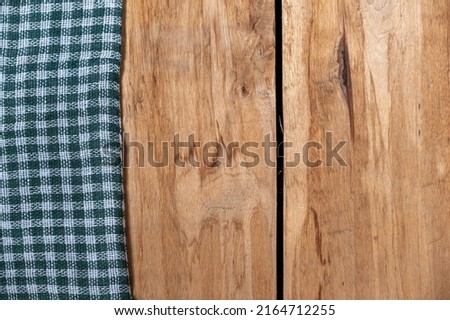A green checkered cloth lies against a wooden background. A towel or kitchen napkin on the rough boards or kitchen table.