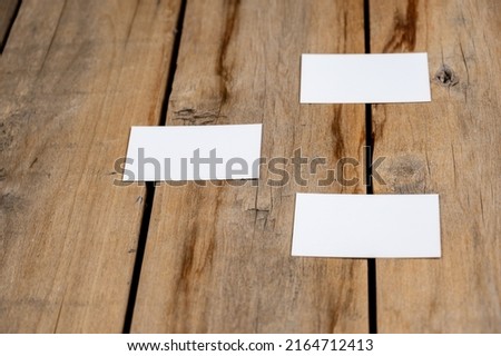 Three Blank business cards against a wooden background. White paper rectangles lie on top of old cracked boards. Selective focus.