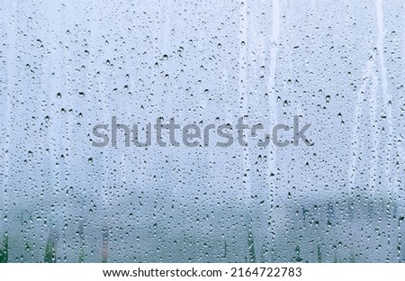 Rain drop on glass window at day time in monsoon season with blurred background. Royalty-Free Stock Photo #2164722783