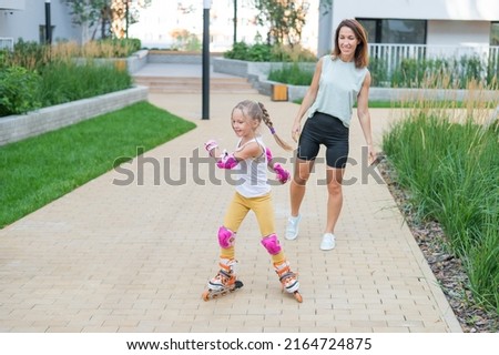 Caucasian woman teaches her daughter to skate on roller skates.