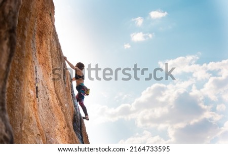 A woman climbs a rock against a blue sky, a strong girl trains strength and endurance, an extreme sport, rock climbing on natural terrain, a rock climber climbs with a rope Royalty-Free Stock Photo #2164733595