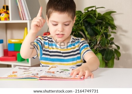 A happy boy of 4 years old looks at a book with pictures, shows pictures and names them.