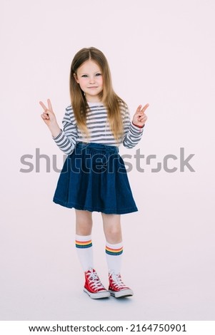 little caucasian kid girl wearing trendy sweater over white background smiling with happy face winking at the camera doing victory sign. Number two.