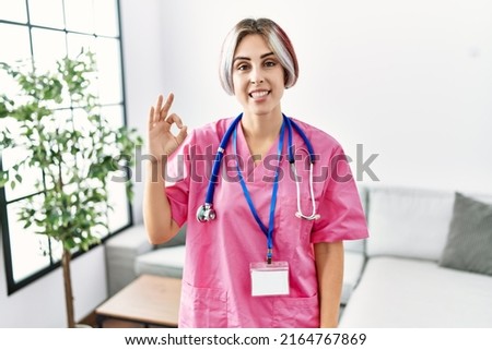 Young beautiful woman wearing doctor uniform and stethoscope smiling positive doing ok sign with hand and fingers. successful expression. 