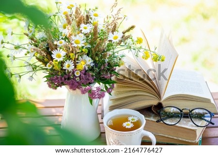 Bouquet of meadow flowers, croissant, cup of tea or coffee, books on table in summer garden. Rest in garden, reading books, breakfast, vacations in nature concept. Summertime in garden on backyard Royalty-Free Stock Photo #2164776427