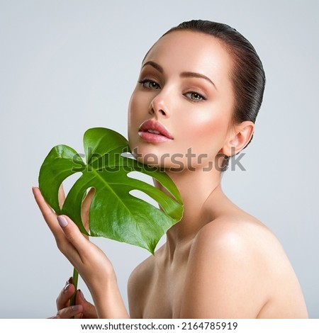 Young beautiful woman with green leave near face and body. Skin care beauty treatments concept.  Closeup girl's face with green leave. White model with clean, health skin of face - posing at studio Royalty-Free Stock Photo #2164785919
