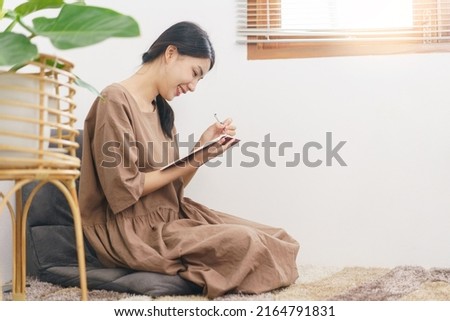 Relaxation lifestyle concept, Young Asian woman writing on notebook while sitting in living room.