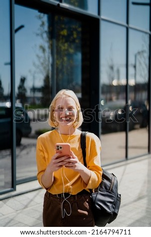 Young happy woman listening music outdoors. Positive blonde girl with headphones enjoying in sunny day	