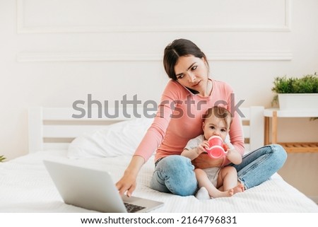 Remote business. Busy young mom with baby working with laptop and smartphone at home, woman using laptop and talking on phone while taking care of baby, free space Royalty-Free Stock Photo #2164796831