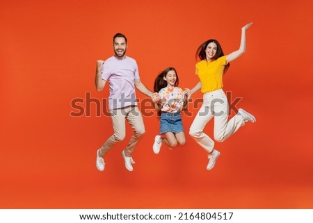 Full body excited young happy parents mom dad with child kid daughter teen girl in basic t-shirts do winner gesture clench fist isolated on yellow background. Family day parenthood childhood concept.