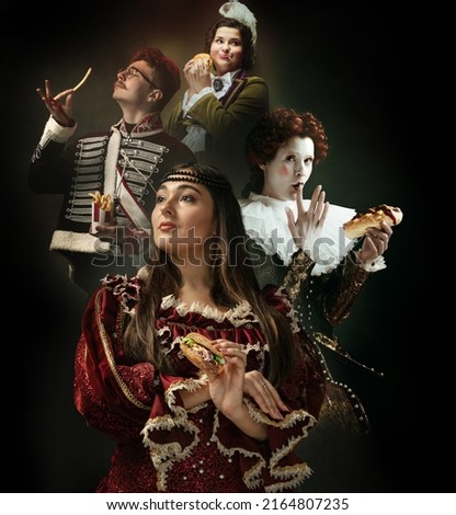 Favorite fast food tastes. Medieval people as a royalty persons in vintage clothing eating fast food on dark background. Concept of comparison of eras, modernity and renaissance style. Creative Royalty-Free Stock Photo #2164807235